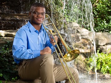 Portrait of Bernard Ekwuazi with his trombone in front of a waterfall background